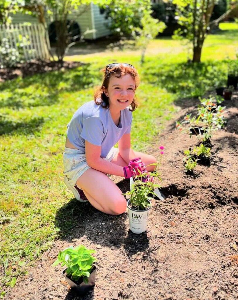 Harper crouched in the garden, planting starters while wearing gloves in the sunshine.